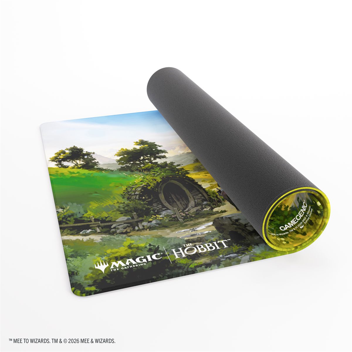 A Magic: The HoBBit gaming mat shown partially rolled, with the unrolled section displaying a green landscape illustration and the Magic: The HoBBit logo. The rolled portion reveals a dark gray underside with a yellow-green edge and the words GAMEMASTER.